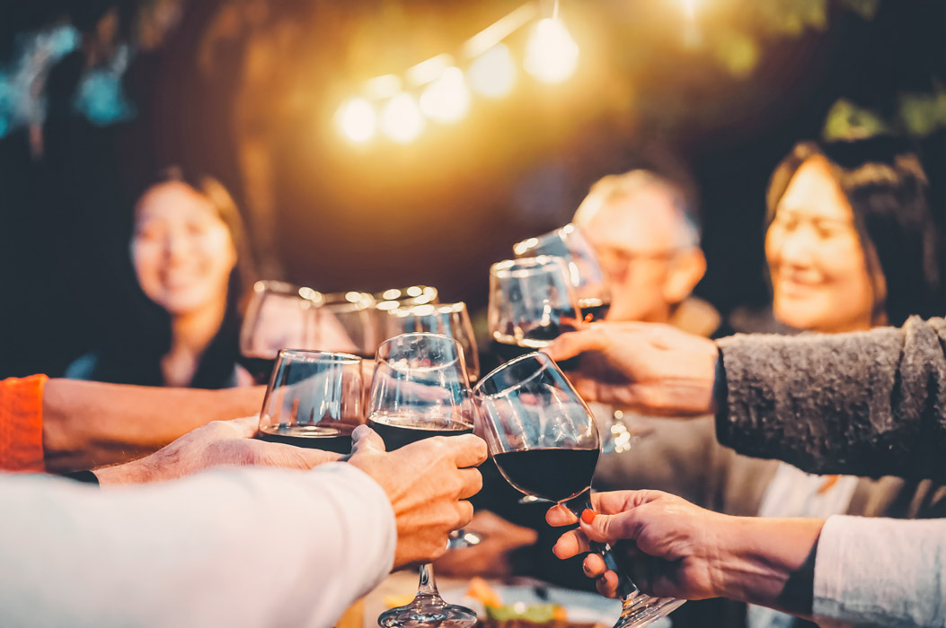 Happy family cheering with red wine at reunion dinner in garden - Senior having fun toasting wineglasses and dining together outdoor - People and food lifestyle concept