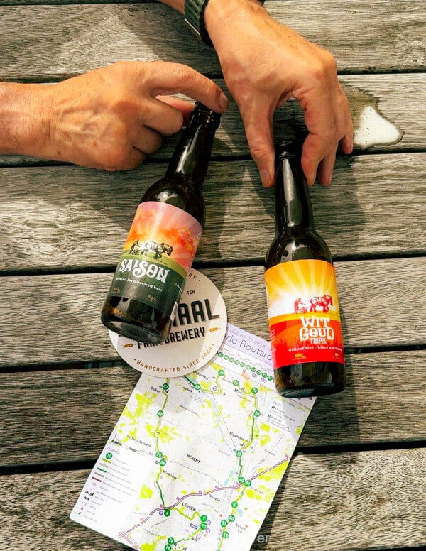 Holding Hof ten Dormaal Saison and Wit Goud bottles over a map of the Dieric Bouts cycle route