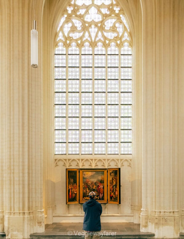 A visitor studying a triptych beneath the vast Gothic window of Sint-Pieterskerk in Leuven