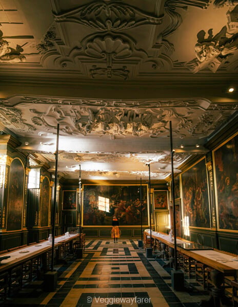 The refectory at Park Abbey in Heverlee, lined with large paintings beneath an ornate stucco ceiling