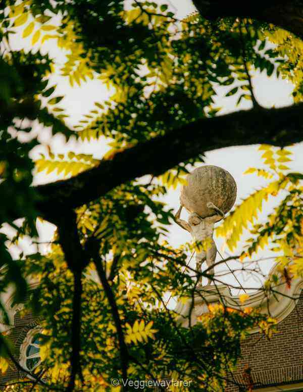 Statue of man holding up the earth (atlas) shot through the leaves of a tree in Nieuwegracht Utrecht