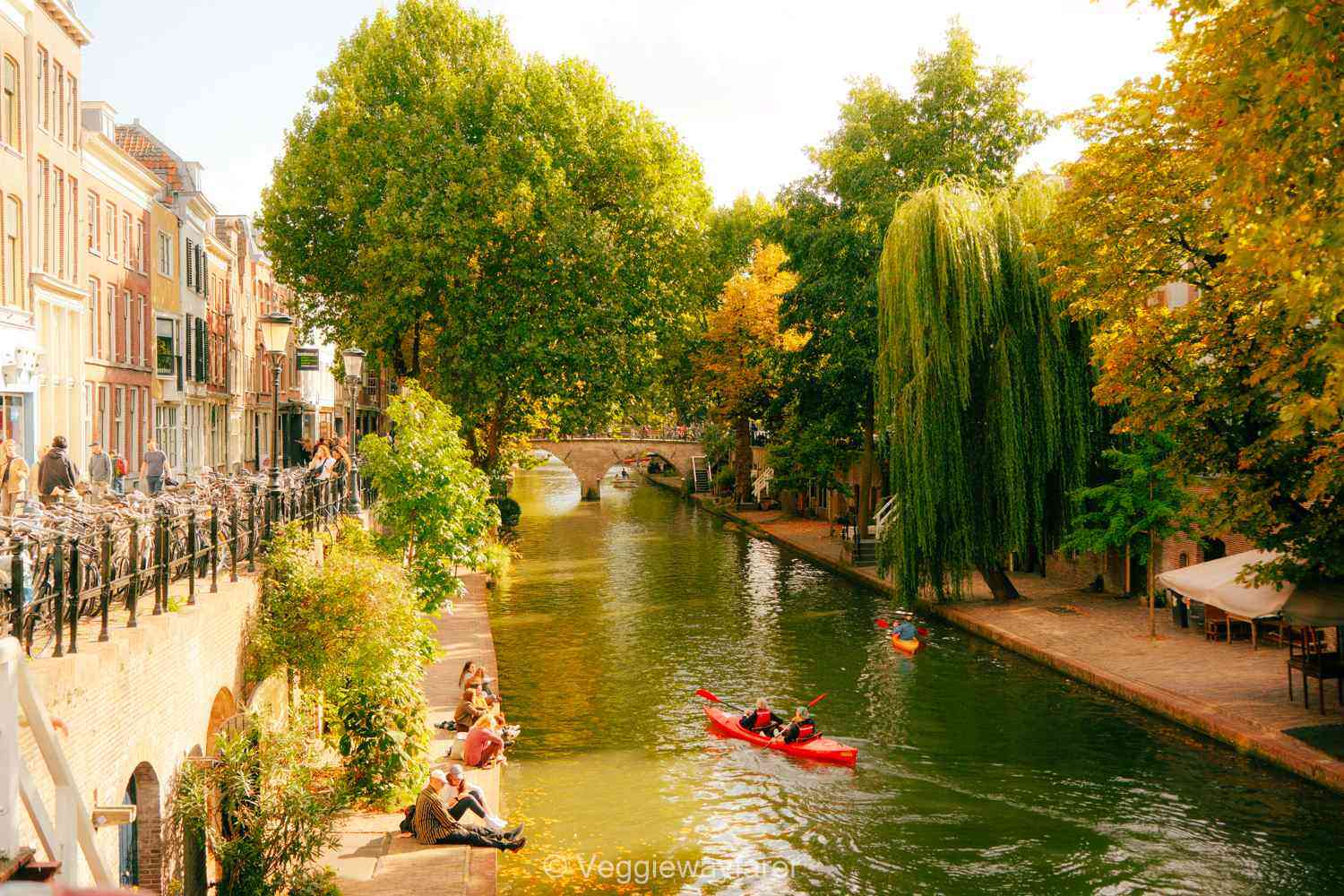 oudegracht in Netherlands. People sitting on the warves and kayakers peddling through the water in a red kayak